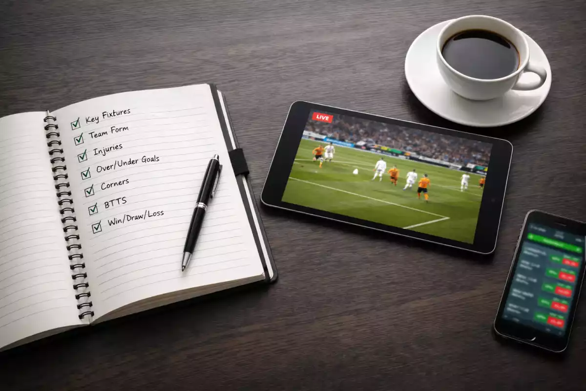 Professioneller Schreibtisch eines Sportwetten-Analysten von oben mit Notizbuch, Tablet und Smartphone für strategische Planung
